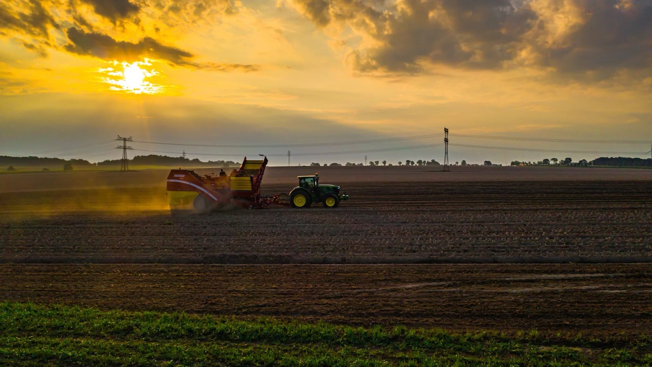 Bestelltes Feld mit Traktor und Pflug im Sonnenuntergang.
