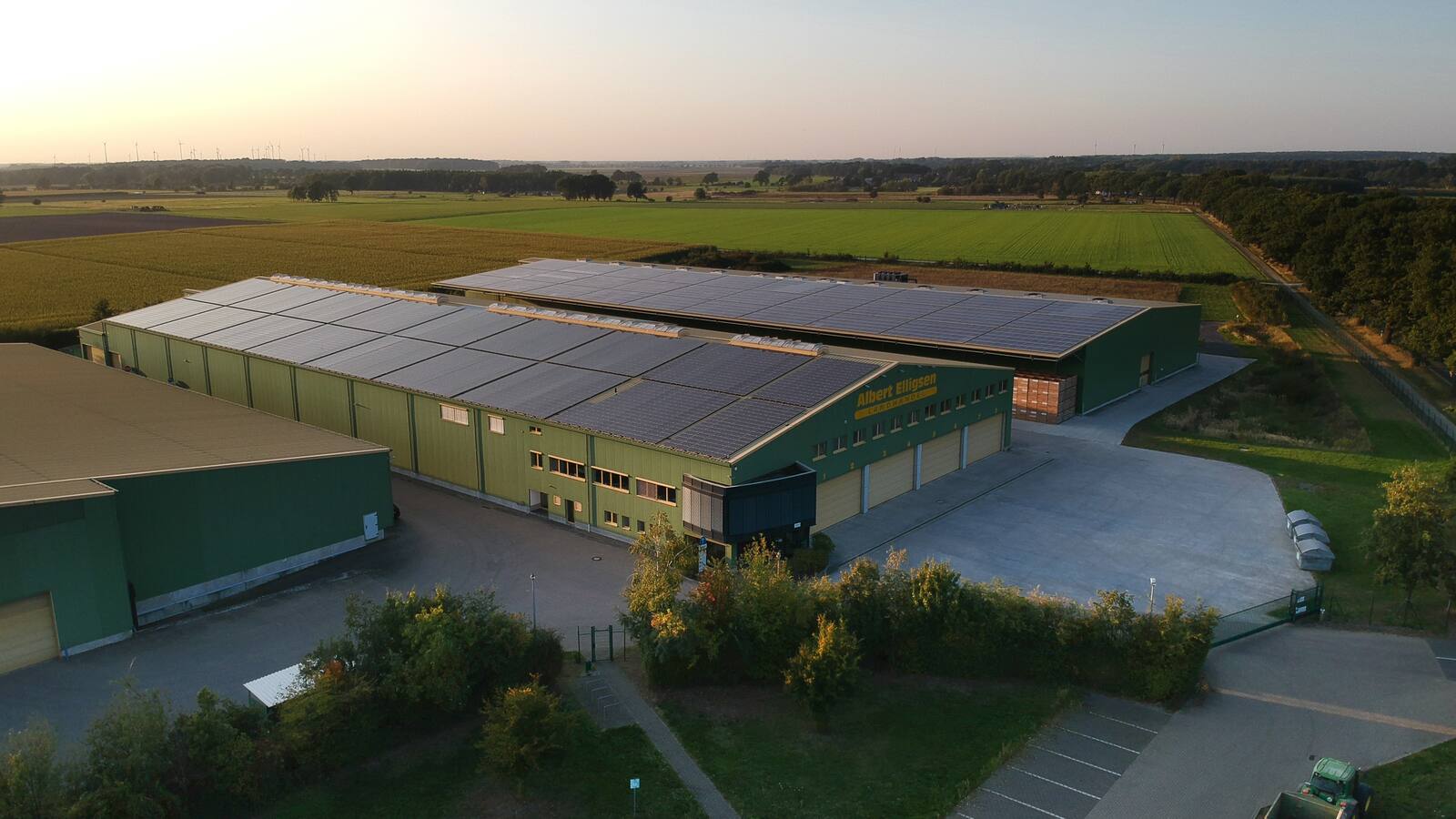 Drei große Lagerhallen umgeben von grünen Feldern.