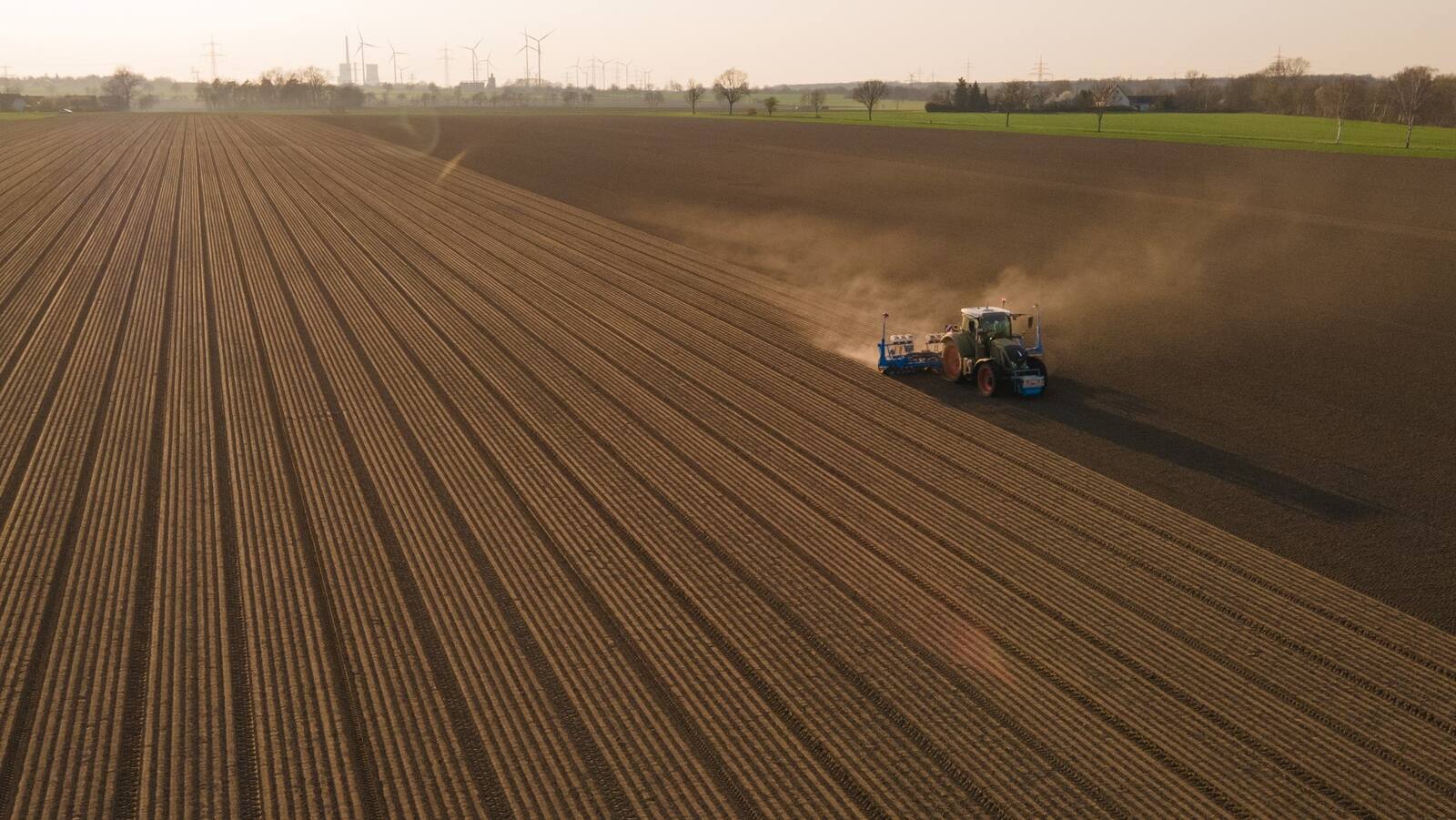 Ein Traktor pflügt ein großes Feld mit staubiger, brauner Erde.