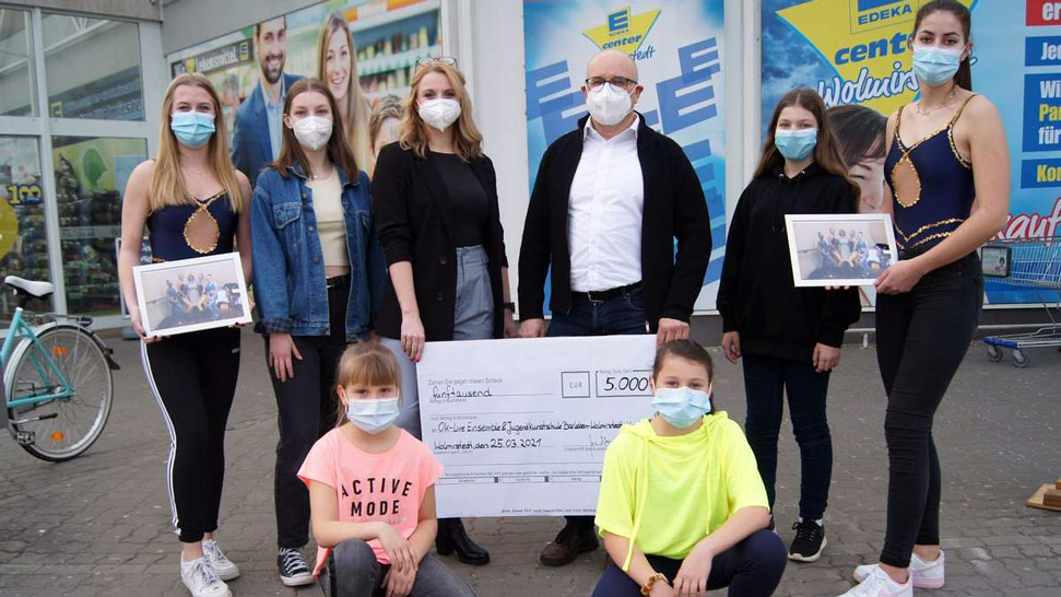 Das Bild zeigt ein Mitglieder des OK Live Ensembles und der Jugendkunstschule Barleben-Wolmirstedt e.V. vor dem EDEKA center Wolmirstedt mit einem Spendenscheck über 5.000€