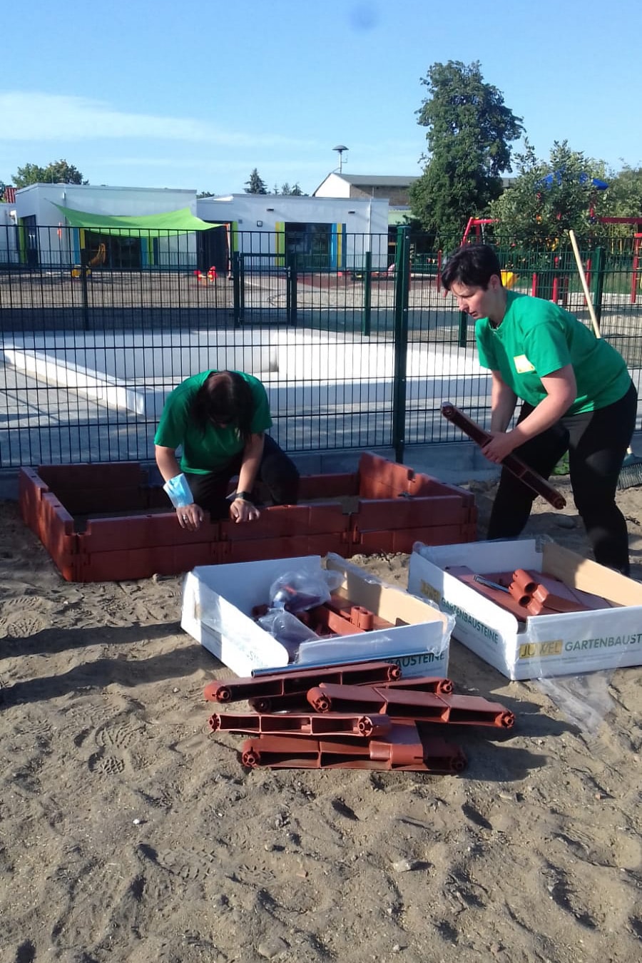 Das Bild zeigt zwei Mitarbeitende des Marktes in grünen T-shirts wie sie ein Gemüsebeet zusammenstecken.