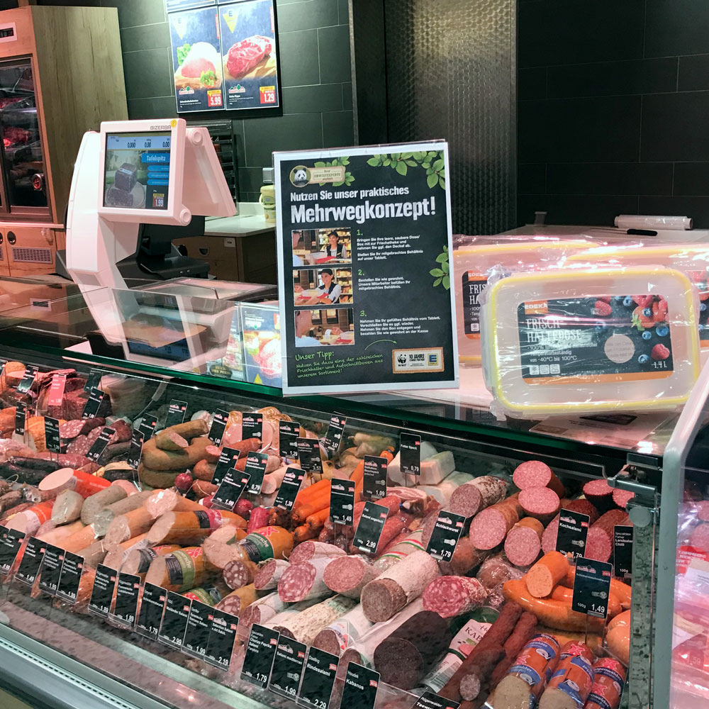 Das Bild zeigt einen Aufsteller auf der Wurst-Bedientheke der für das Mehrwegkonzept wirbt.
