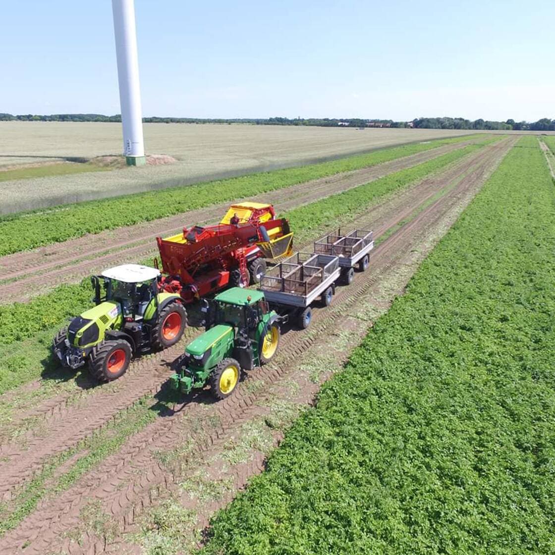 Zwei Traktoren fahren mit Anhängern über ein Feld.
