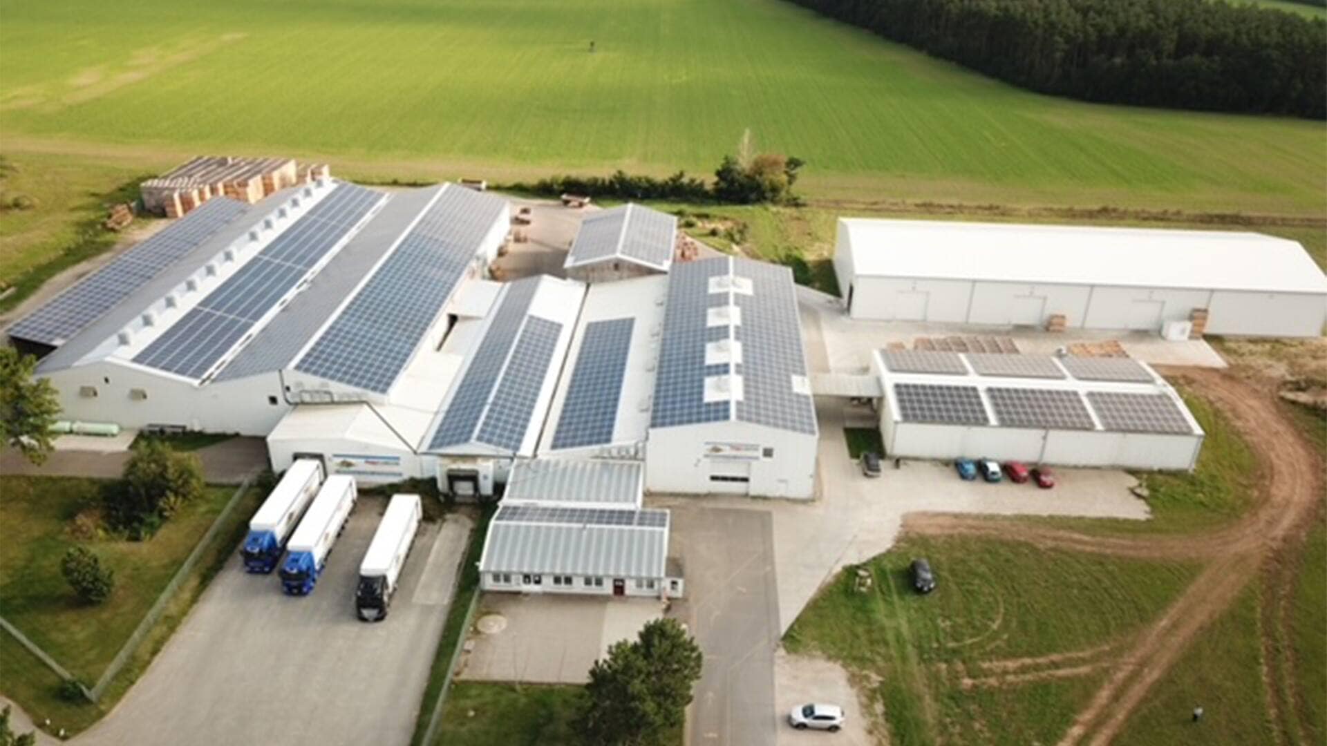 Luftaufnahme eines weißen ländlichen Gebäudekomplexes. Die Dächer sind mit Solarzellen ausgestattet.