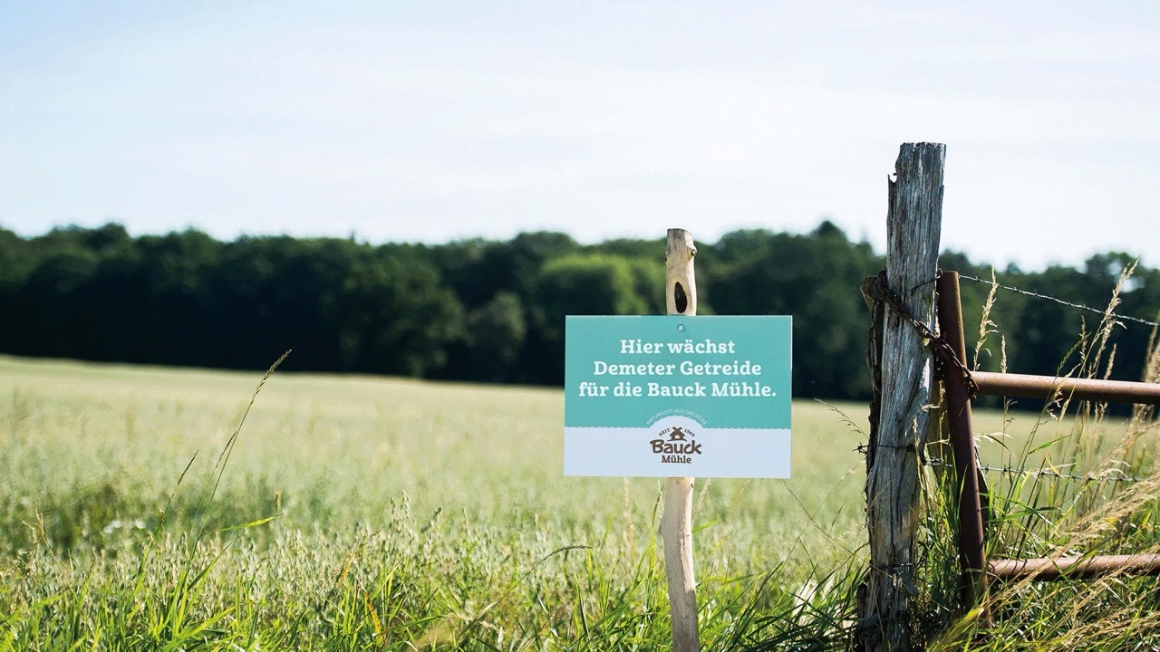 Am Zaun vor dem Feld steht ein Schild mit der Aufschrift: Hier wächst Demeter Getreide für die Bauck Mühle.