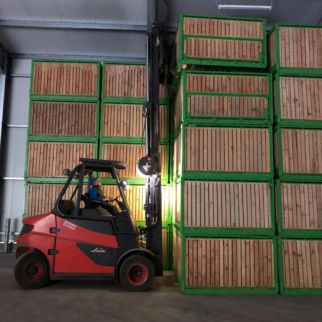 Ein roter Stapler hält vor einem Turm aus Containerpaletten.