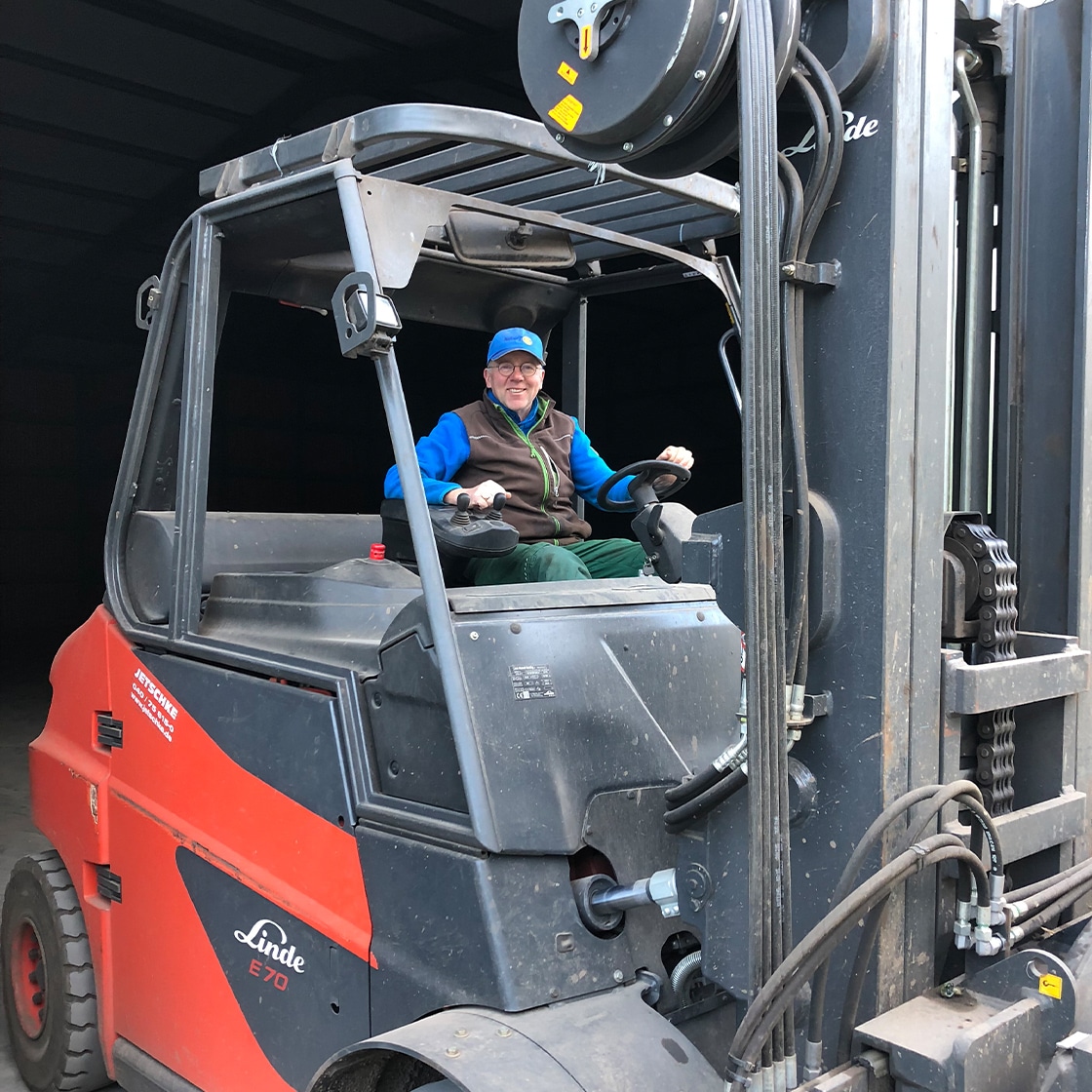 Ein Mann sitzt auf einem landwirtschaftlichem Fahrzeug und lächelt. Er trägt eine blaue Mütze.