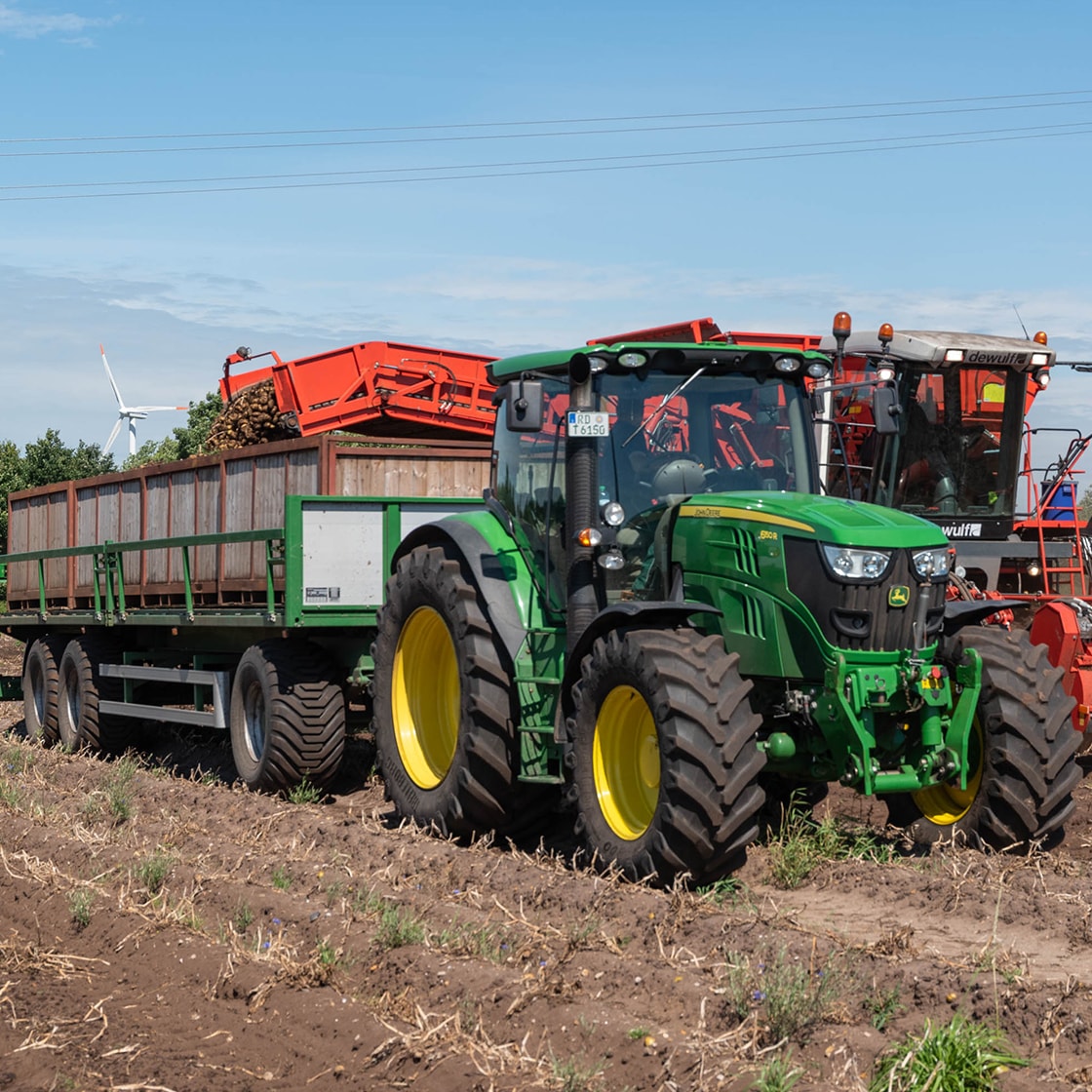Ein grüner Traktor mit Anhänger auf einem Feld.