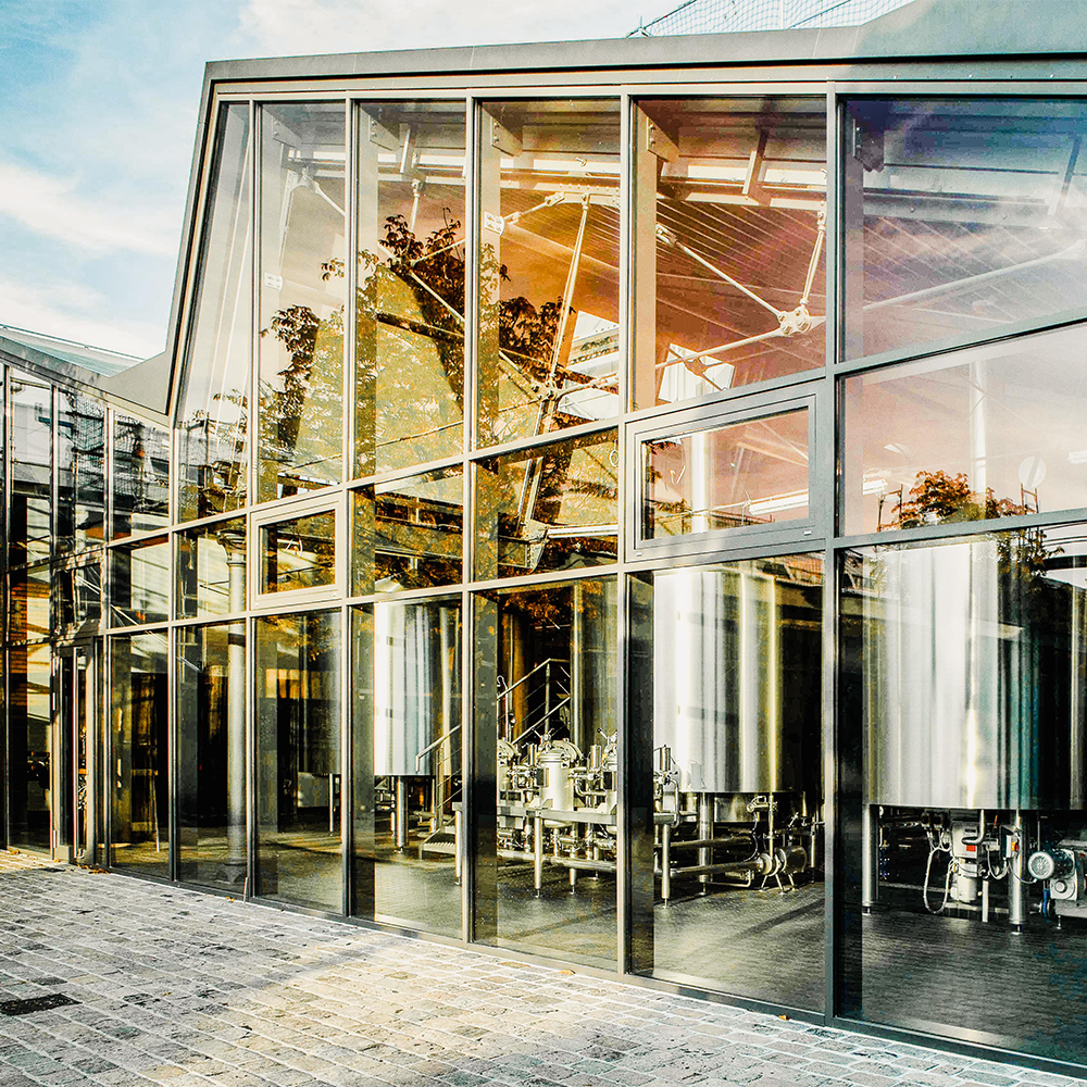 Große Braukessel aus Edelstahl hinter einer modernen verglasten Fassade.