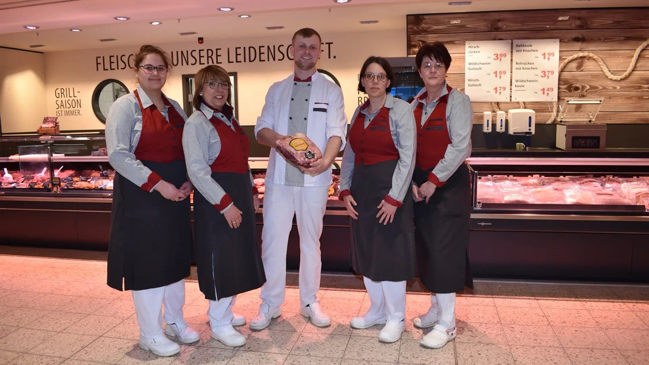 Fünf Personen in Fleischerei Arbeitskleidung stehen vor der Fleischtheke.