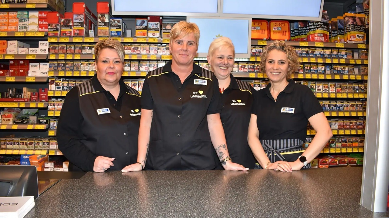 Vier Frauen in schwarzer EDEKA-Kleidung stehen hinter einem Bedientresen. Hinter ihnen diverse Tabakprodukte.