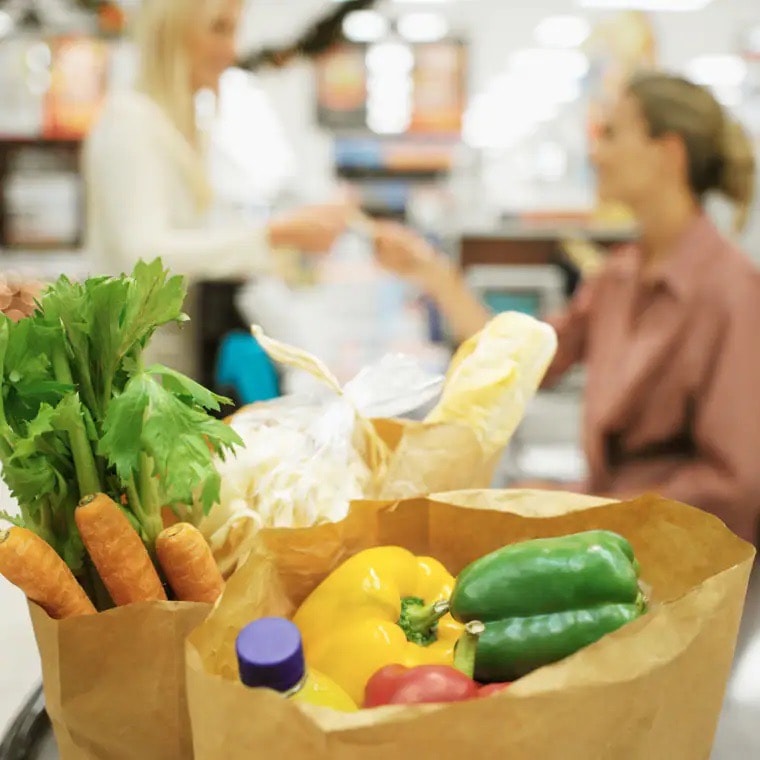 Zwei Papiertüten mit Lebensmitteln wie Möhren, Paprika und Wasser.