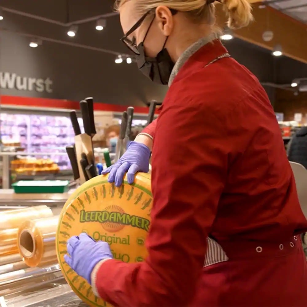 Eine Frau mit Mund-Nasen-Schutzmaske hält einen Laib Käse.