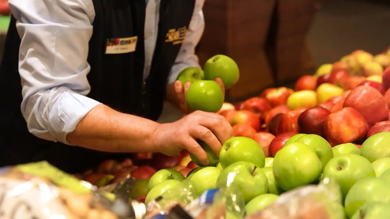 Ein Person nimmt grüne Äpfel aus dem Obstregal.