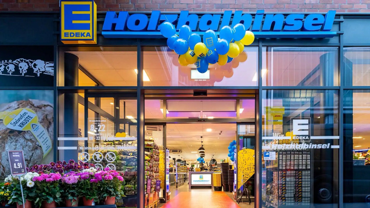 Eingang des EDEKA Holzhalbinsel mit blauen und gelben Ballons. Vor dem Eingang werden Blumen angeboten.