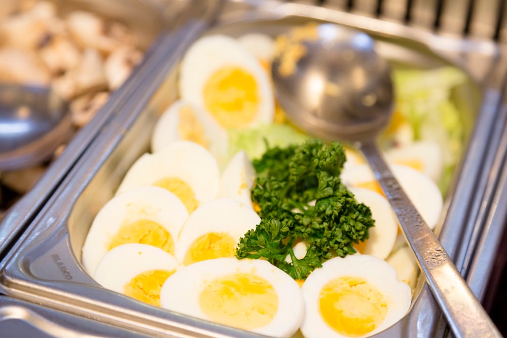 Edelstahl-Behälter mit gekochten und halbierten Eiern.