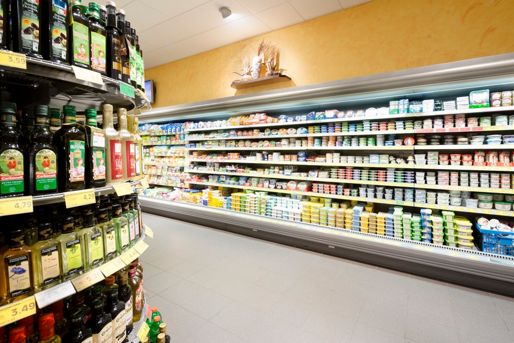 Vor dem Kühlregal mit Butter und Käse stehen verschiedene Essig- und Ölsorten.