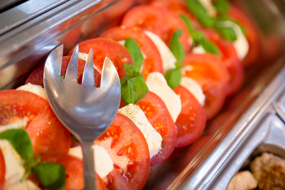 Edelstahl-Behälter der Salatbar mit Tomatenscheiben, Mozzarella und Basilikum.
