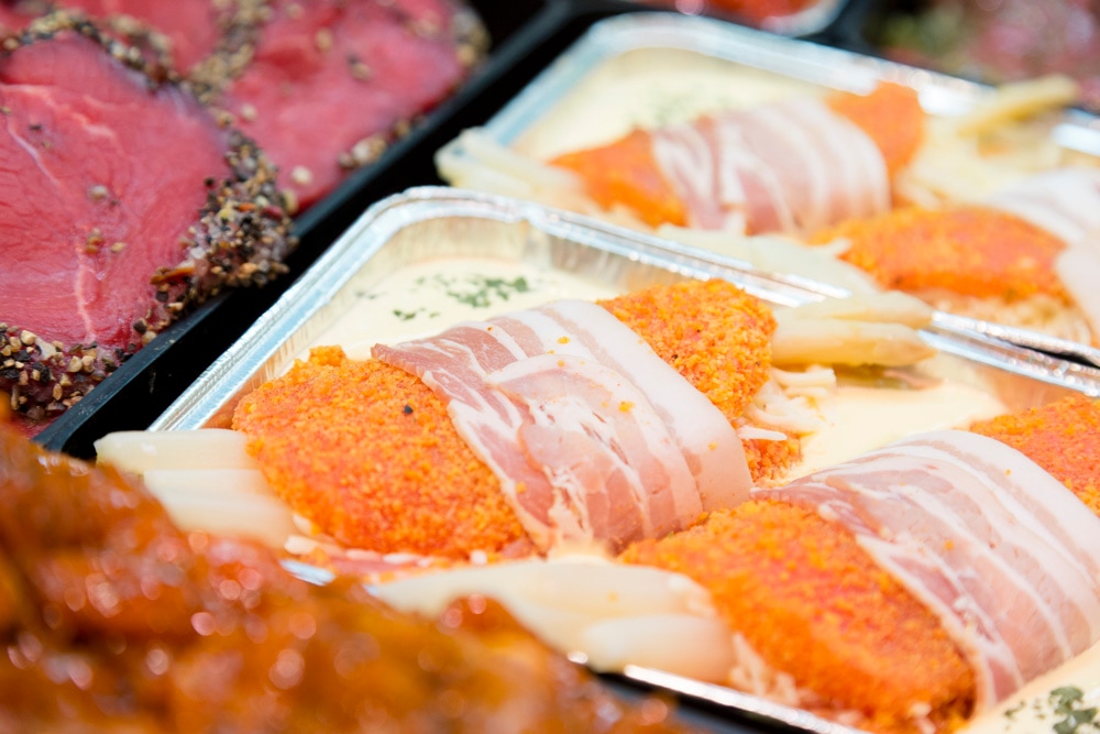 Paniertes Stück Fleisch mit weißem Spargel und Bacon-Mantel.