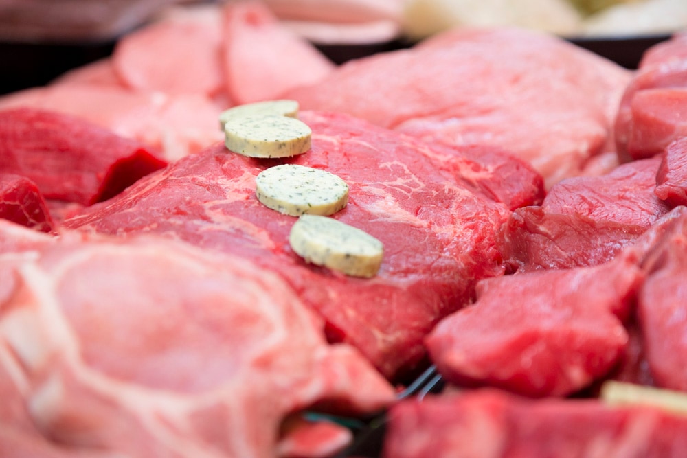 Rohes Stück Fleisch mit Talern aus Kräuterbutter.