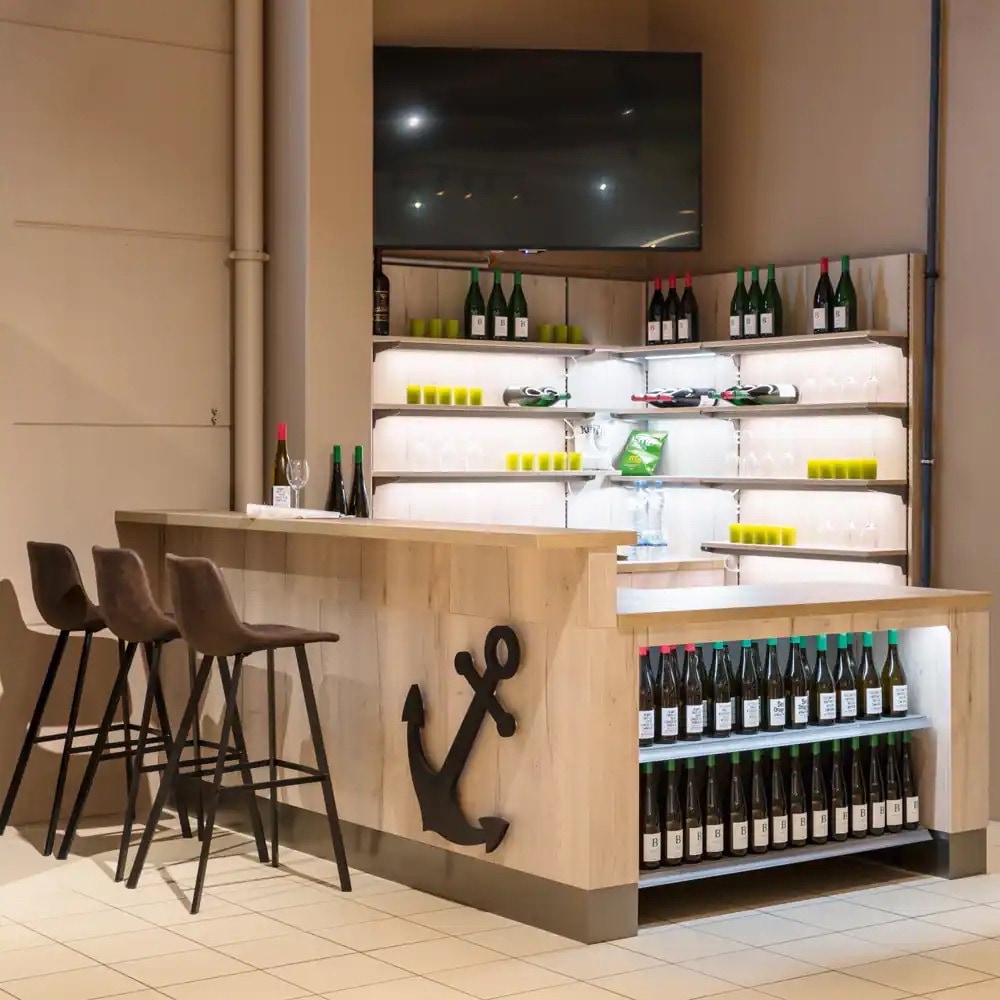 Kleine Weinbar mit Tresen und drei Barhockern. Über dem Weinregal ein großer Fernseher.