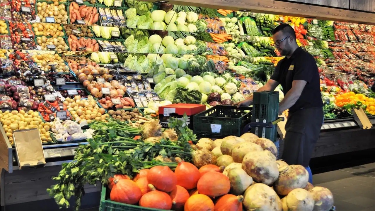 Ein Mann im schwarzen EDEKA-Poloshirt schient leere Gemüsekisten durch die Abteilung.