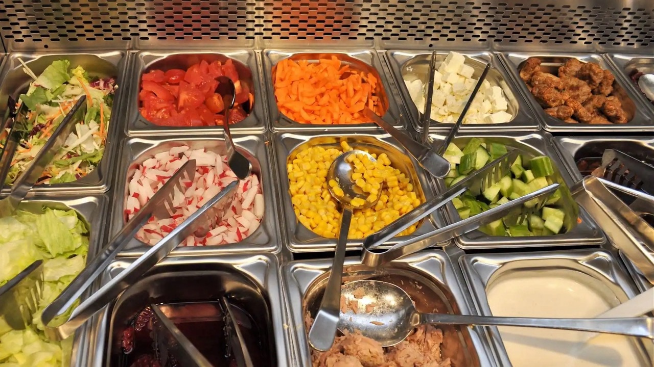 Edelstahlbehälter für Salate mit Tomaten, Möhren, Feta, Radieschen, Mais, Gurken, Thunfisch und Dressing.