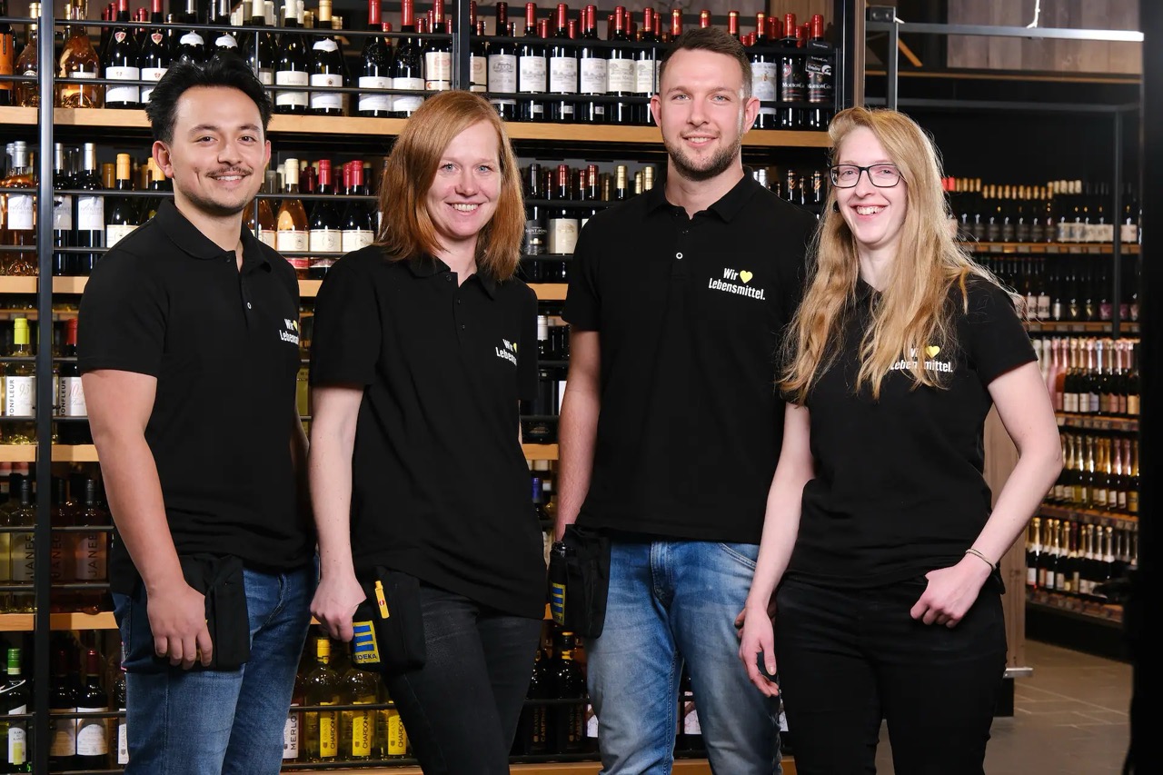 Zwei Frauen und zwei Männer in schwarzen EDEKA-Poloshirts vor einem Weinregal.