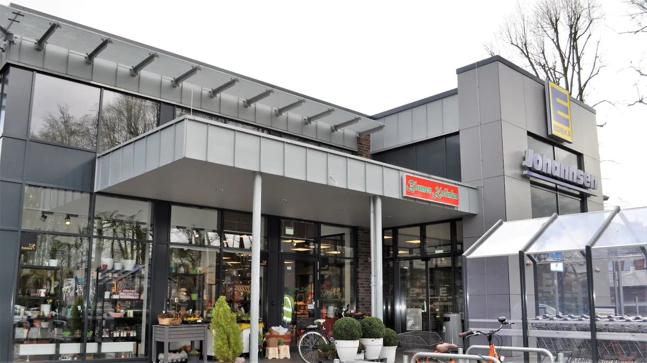 Außenbereich von EDEKA Johannsen mit Eingang zum Blumenladen und überdachtem Einkaufswagen-Parkplatz.
