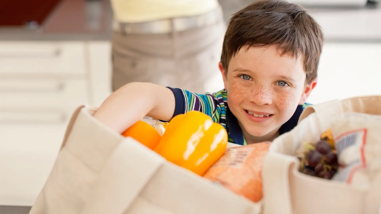 Ein kleiner Junge greift in einen hellen Tragebeutel, aus dem gelbe Paprikas herausragen.