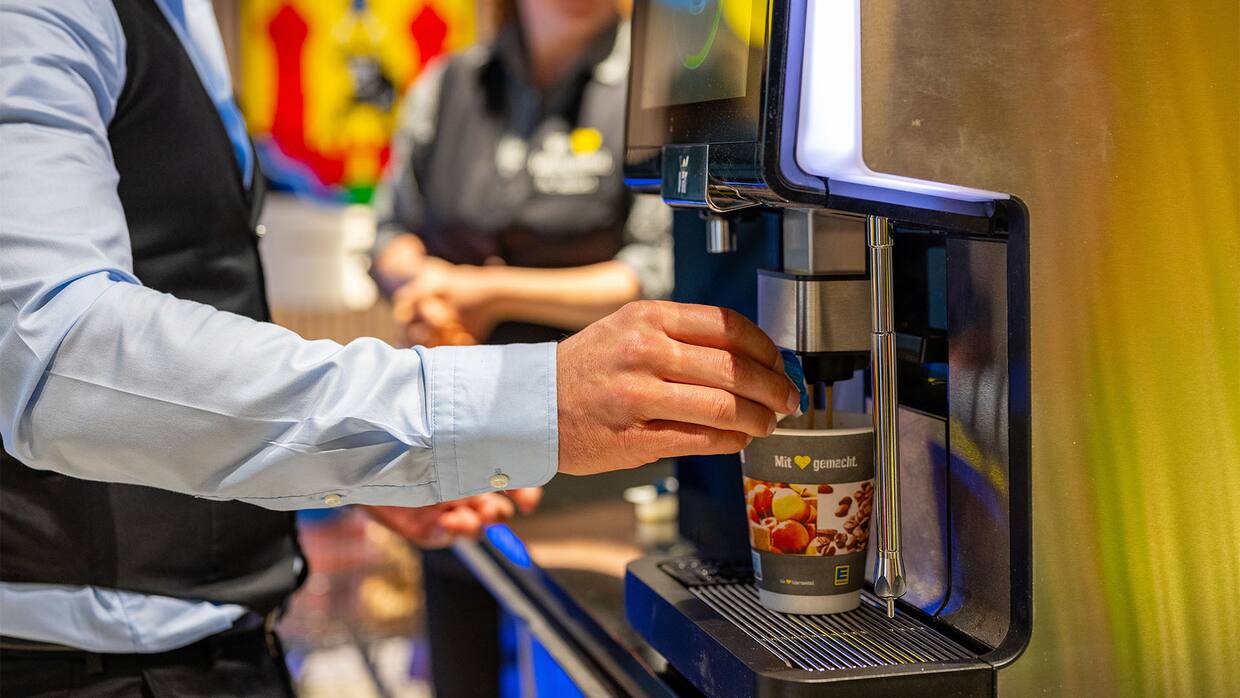 Kaffeemaschine mit EDEKA-Becher darunter.