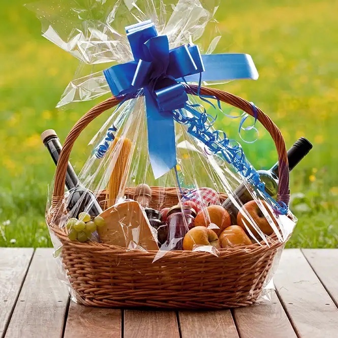 Geflochtener Präsentkorb mit blauer Schleife an der Klarsichtfolie. Im Korb Weinflaschen, Käse und Obst.
