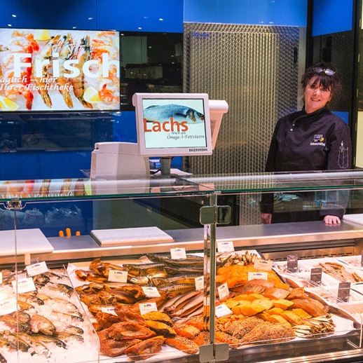 Fischtresen mit schwarz gekleideter Mitarbeiterin und einem Screen an der Wand.