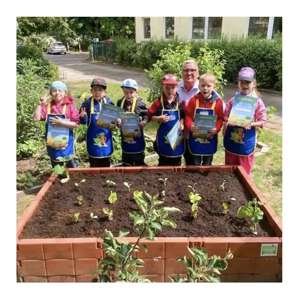 Sechs Kinder und ein Erwachsener stehen an einem Hochbeet.