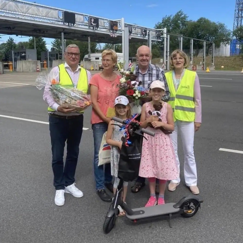 Vier Erwachsene und zwei Kinder mit einem Tretroller stehen auf einer Straße.