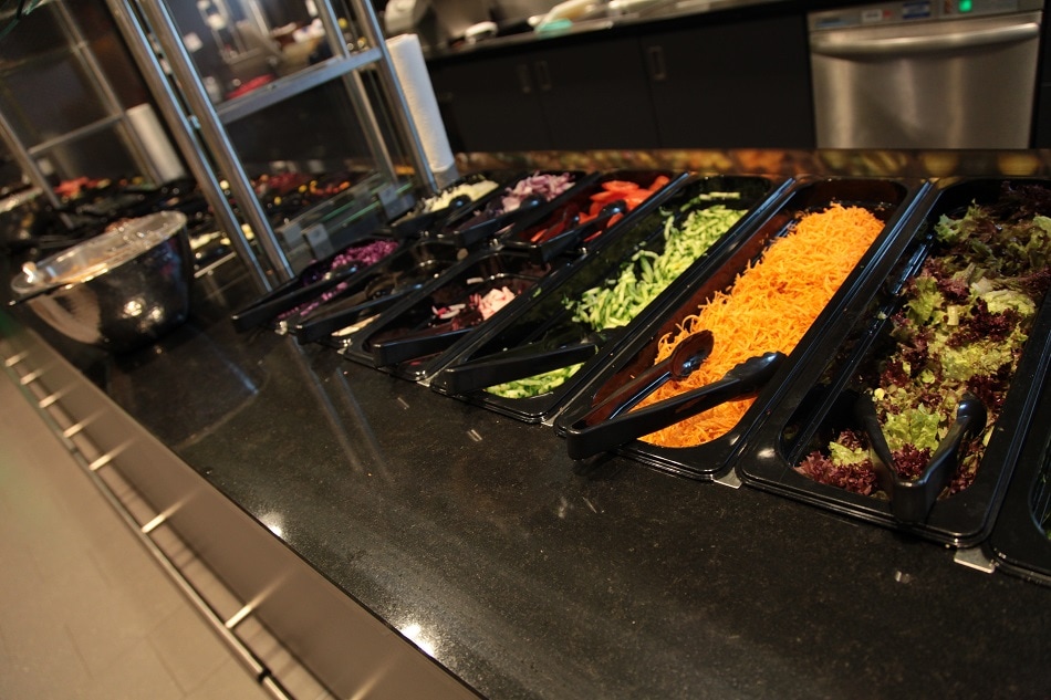 Diverse schwarze Behälter mit Zutaten für einen gemischten Salat.