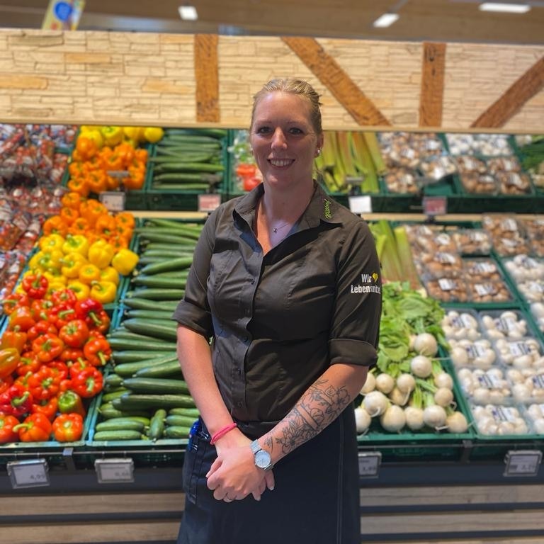 Frau in EDEKA-Kleidung vor dem Gemüseregal.