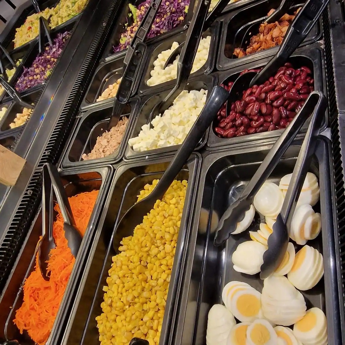 Salatbar mit Metallbehältern voller Ei, Mais, Möhrensalat, Kidneybohnen, Feta und Thunfisch.