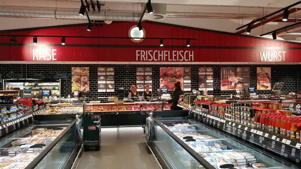 Frischetheke mit roter Wand, auf der Käse, Frischfleisch und Wurst steht.