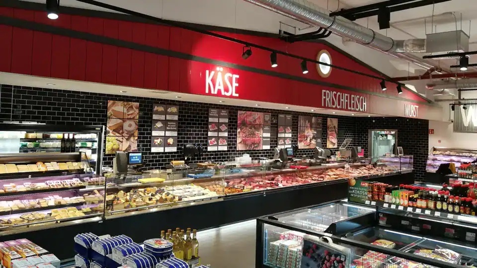 Frischetheke mit roter Wand, auf der Käse, Frischfleisch und Wurst steht.