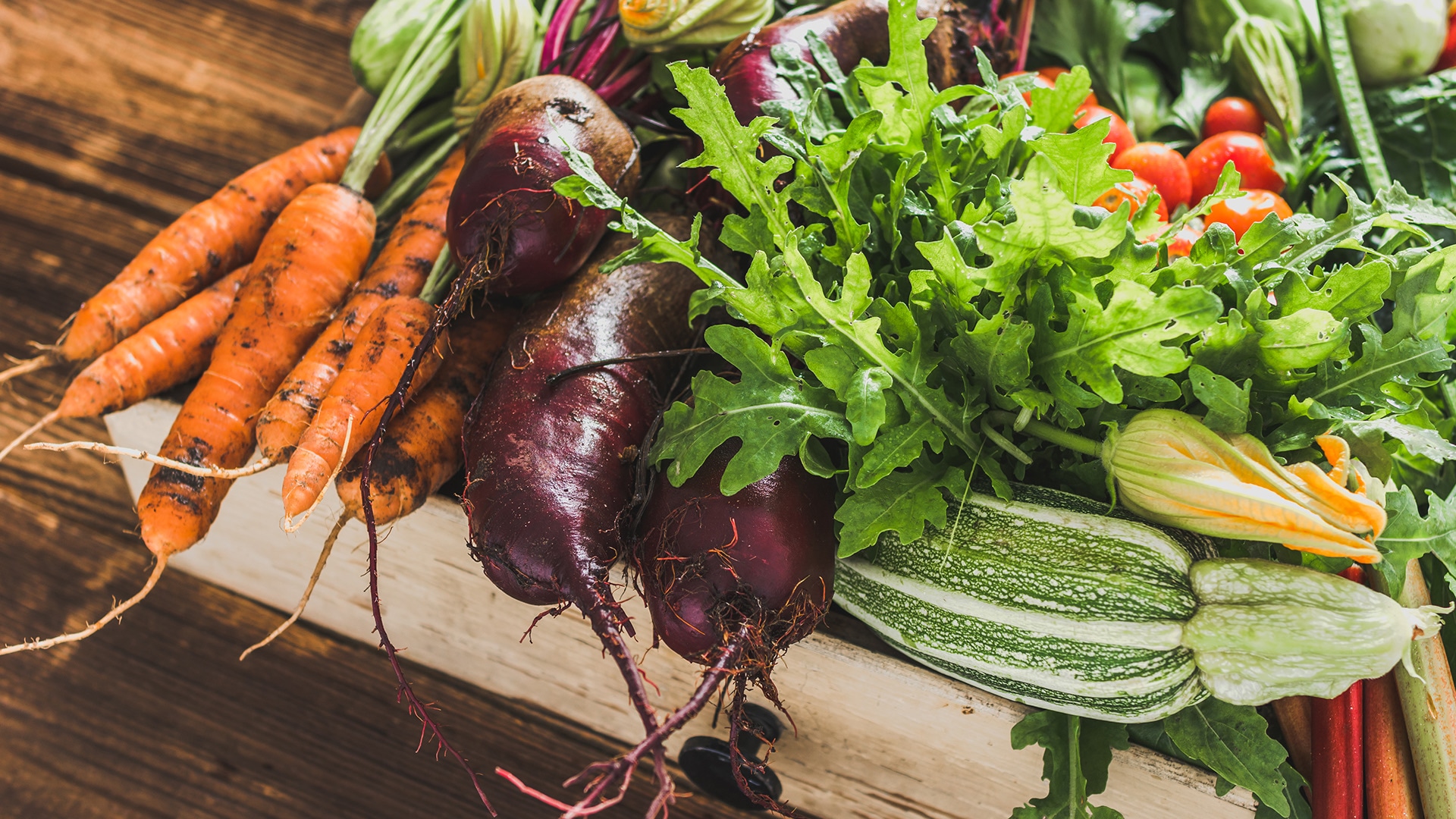 Ein Holzkorb mit verschiedenen frischen Gemüsesorten, teils noch mit Erde bedeckt.