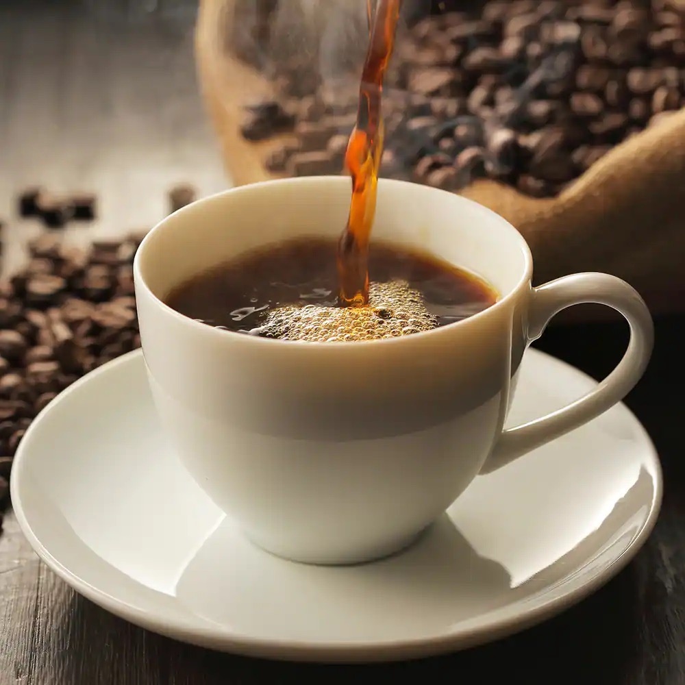 Ein Strahl Kaffee füllt eine weiße Tasse mit Untersetzer.