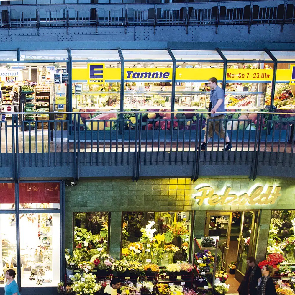 Beleutete Glasfassade von EDEKA Tamme im ersten Stock. Darunter der Blumenladen Petzoldt.