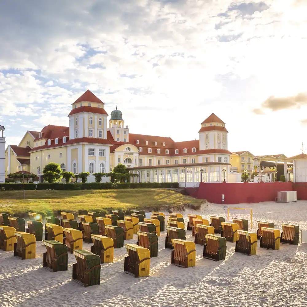 Ein weißes Schloss mit rotem Dach direkt am Strand mit vielen Strandkörben.