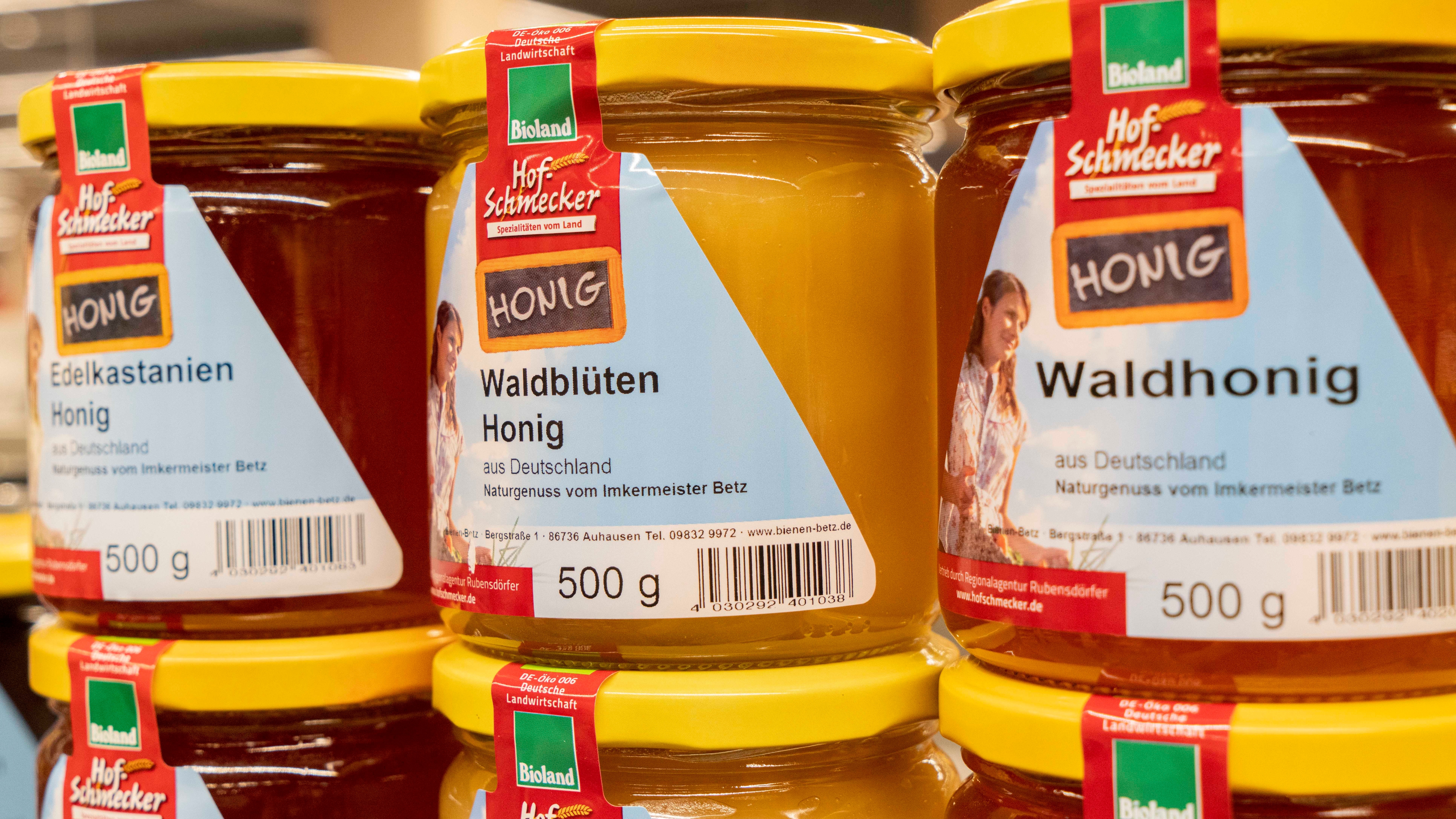Nahaufnahme von regionalem Honig in Gläsern, die nebeneinander stehen. Auf den Etiketten steht "Waldhonig", "Waldblüten Honig" und "Edelkastanien Honig".