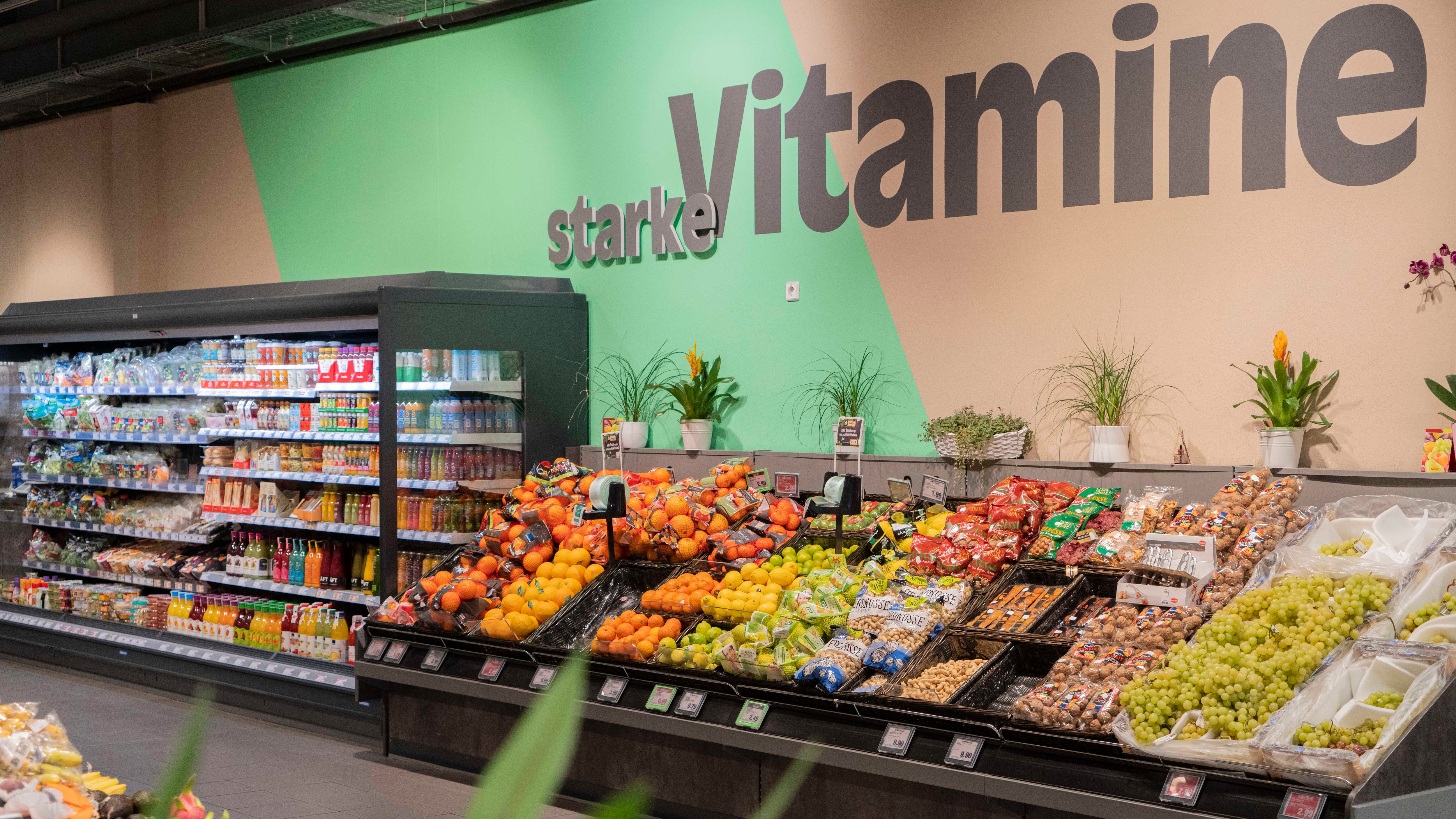 Eine Obsttheke mit verschiedenen Obstsorten in einem Lebensmittelhandel. An der Wand steht starke Vitamine.