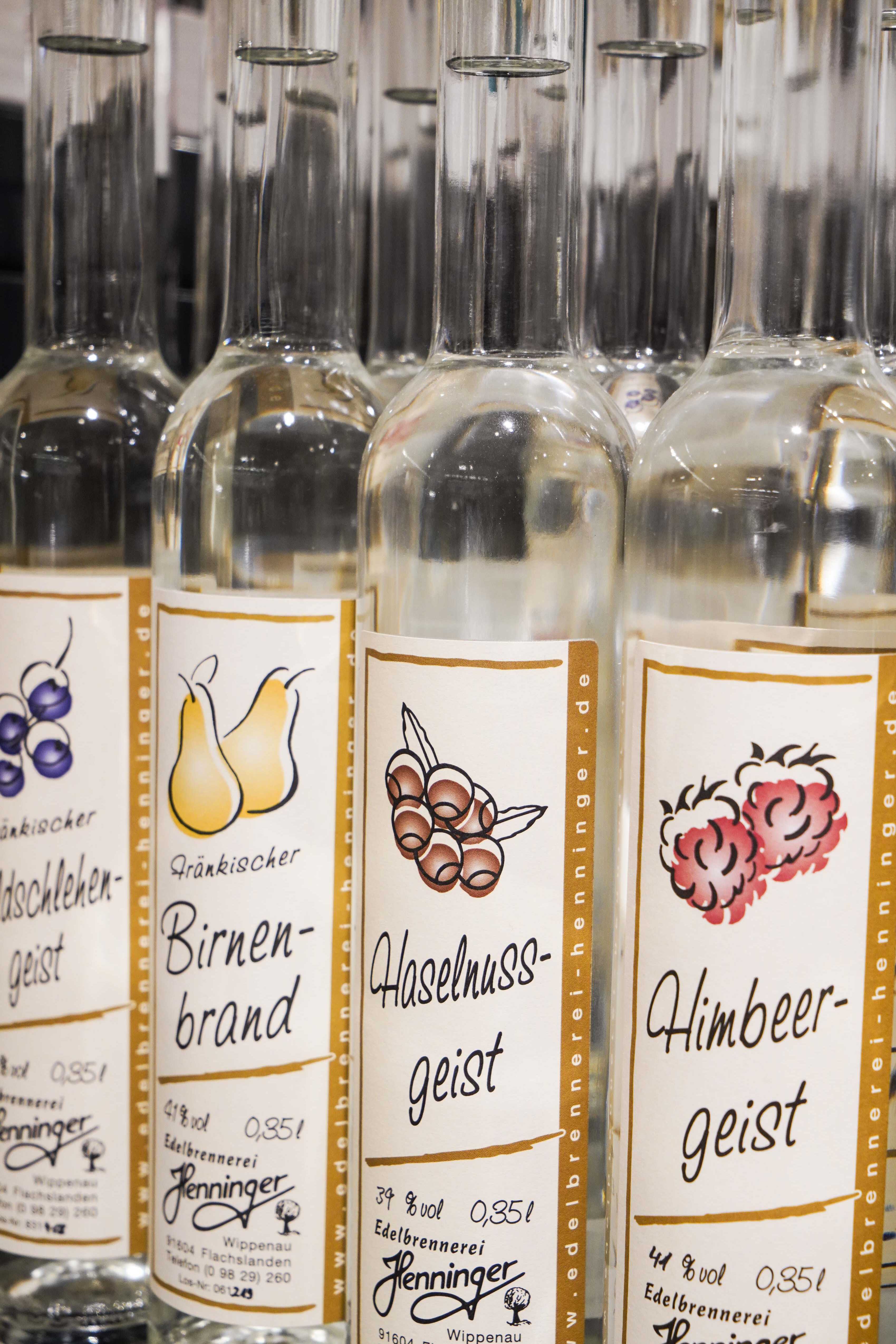 Nahaufnahme von regionalen Spiritousen, die nebeneinander stehen. Auf den Flaschen sind Etiketten auf denen "Himbeergeist", "Haselnussgeist", "Birnenbrand" und "Wildschlehengeist" steht.
