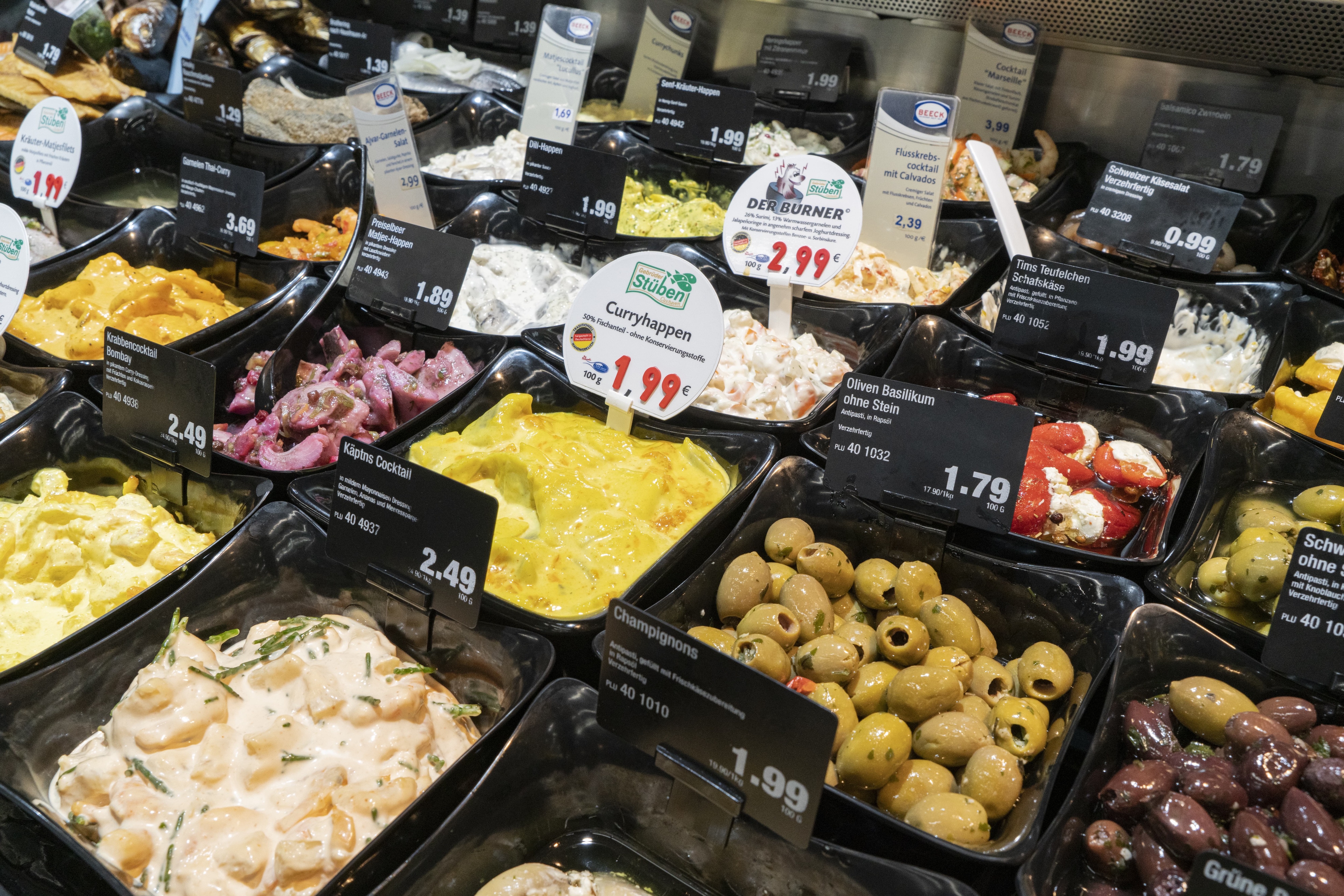 Verschiedene Salate und Antipasti mit Preisschildern in einer Auslage.