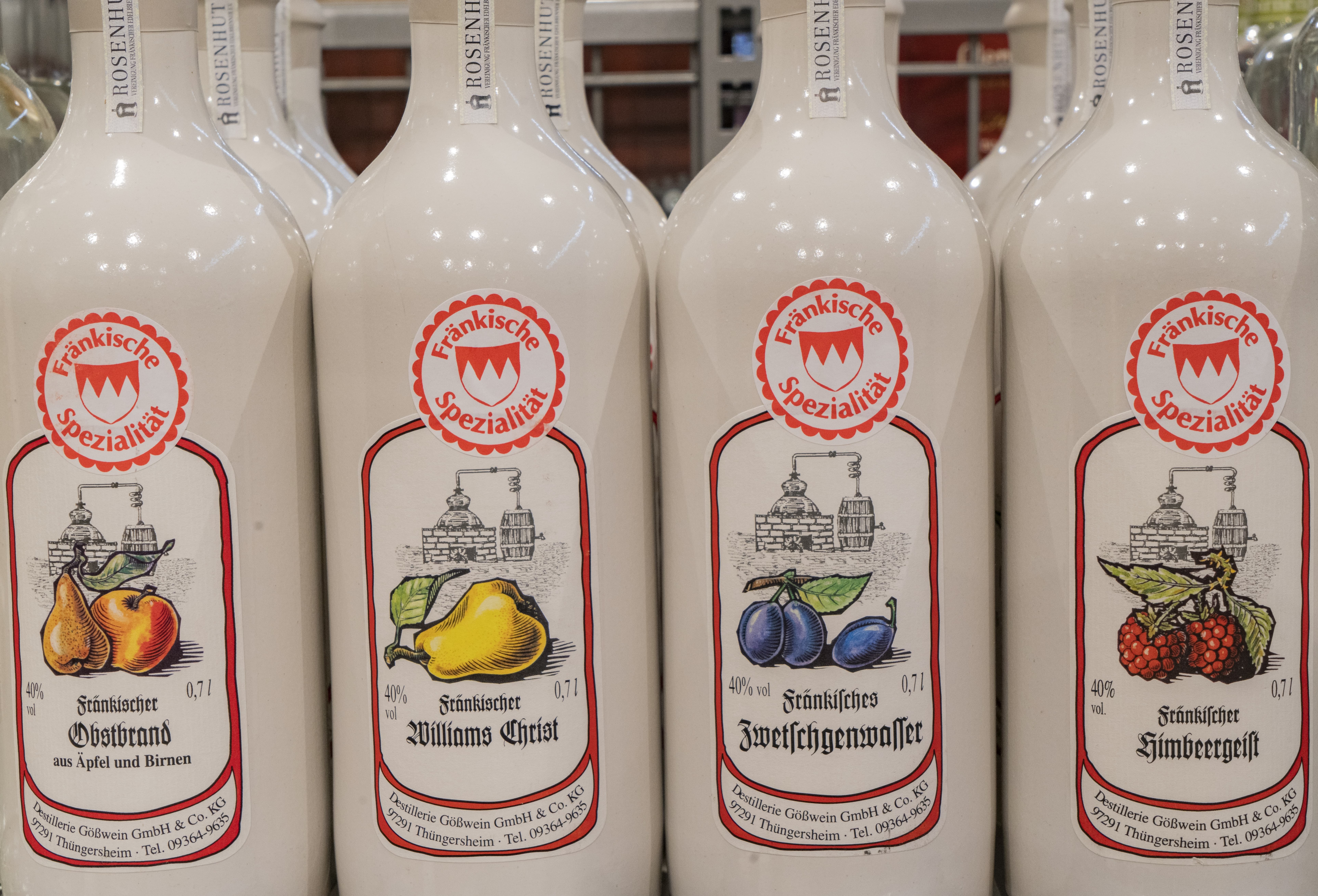Close-Up von vier weißen Spirituosenflaschen mit verschiedenen Etiketten, die sie als regionale Spezialitäten ausweisen.