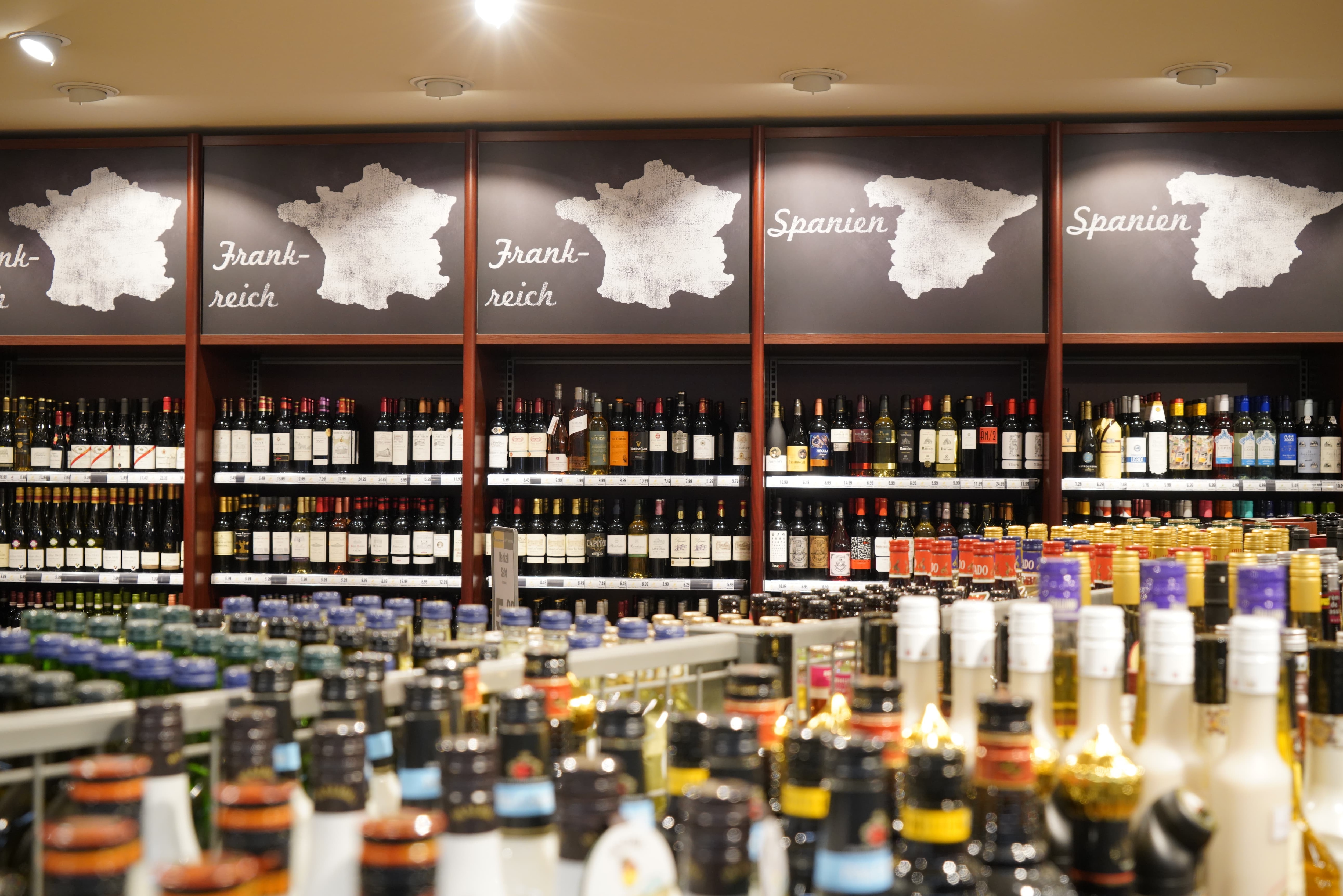 Die Weinabteilung eines EDEKA-Markts. Über den Regalen befinden sich Schilder mit der Aufschrift „Frankreich“ und „Spanien“.